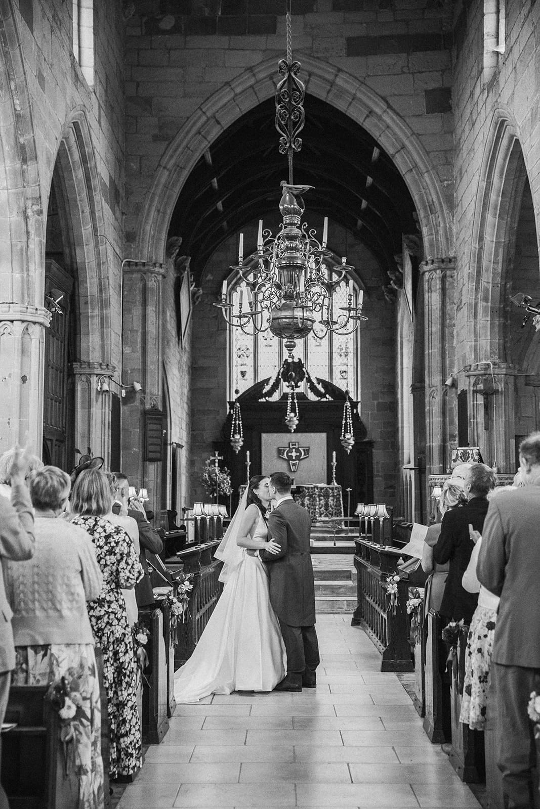 Bride and groom first kiss during wedding ceremony at St Helen’s Church Ashby-de-la-Zouch