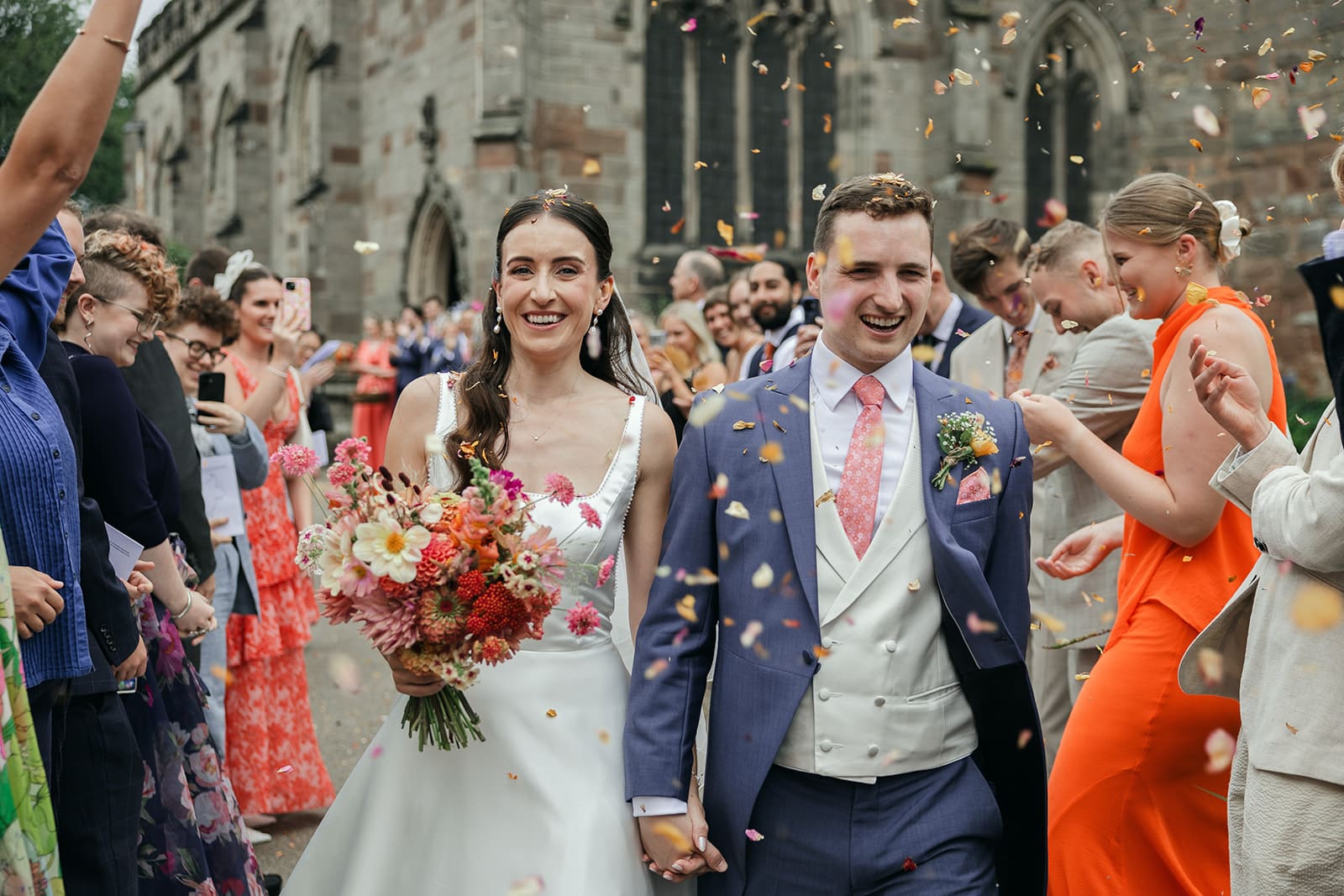Bride and groom walking through confetti outside St Helen’s Church Ashby-de-la-Zouch