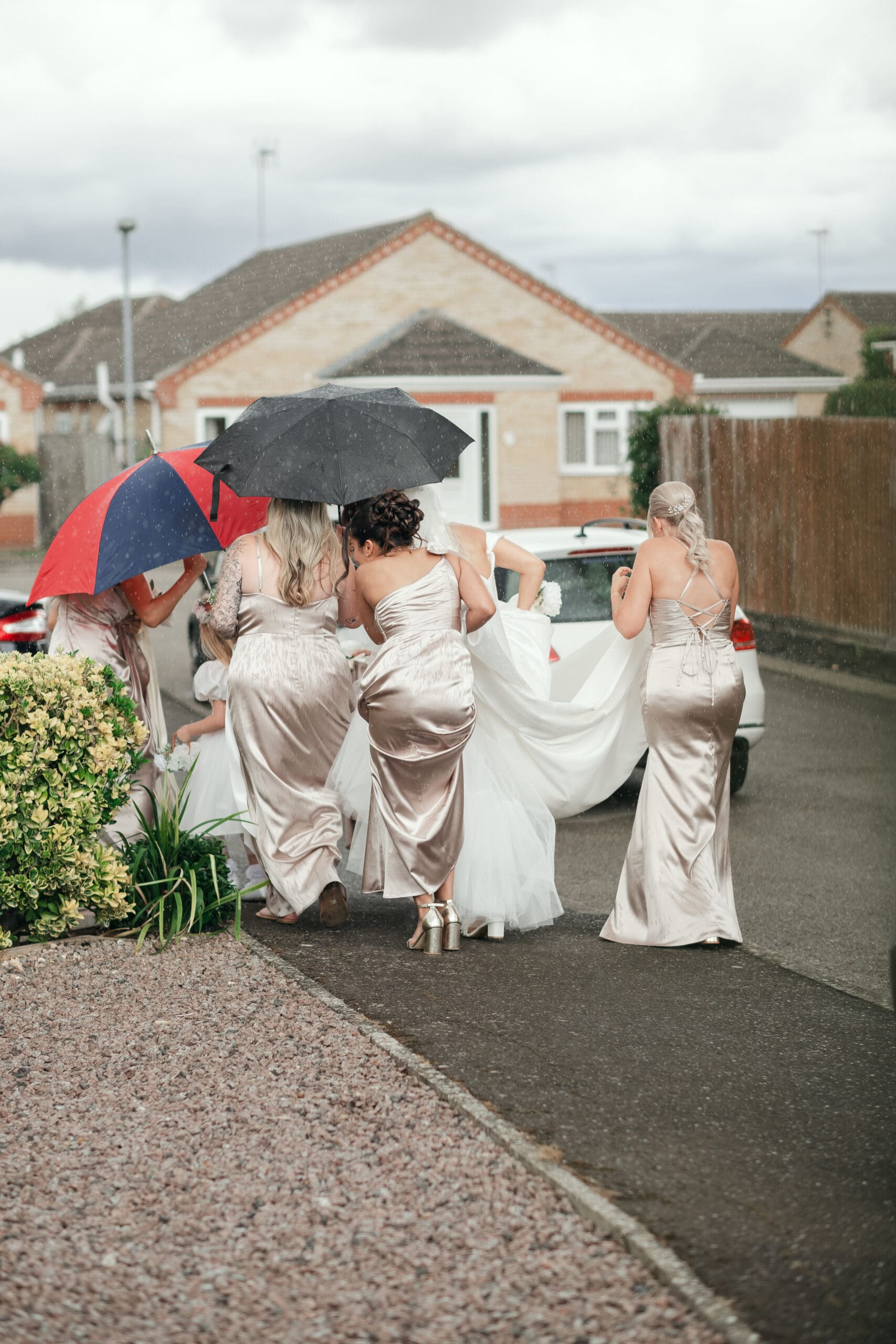 Candid shot of wedding party with umbrellas during rainy summer wedding in Cambridgeshire