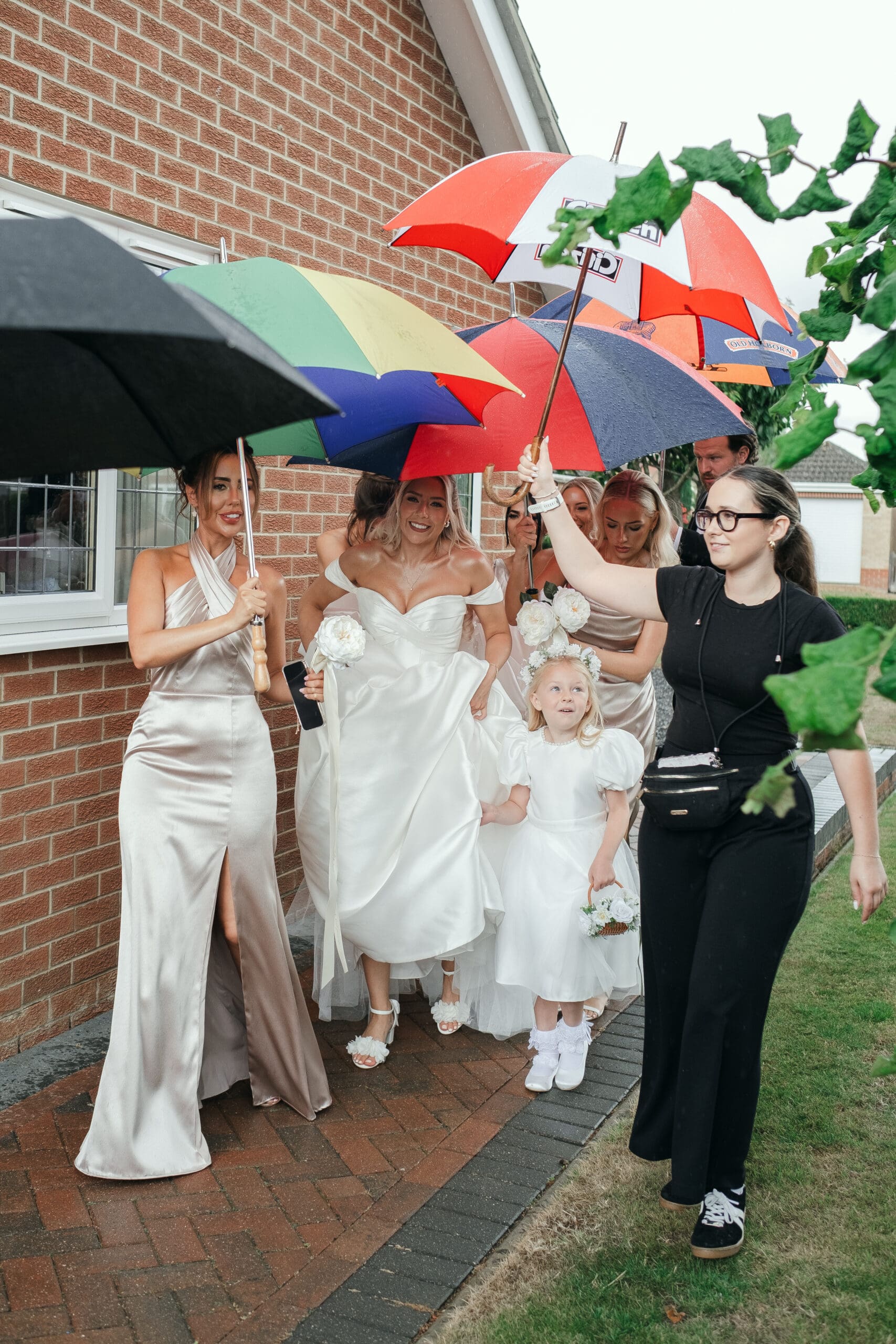 Bride and bridesmaids walking in the rain with umbrellas on their way to St Paul’s Church Gorefield