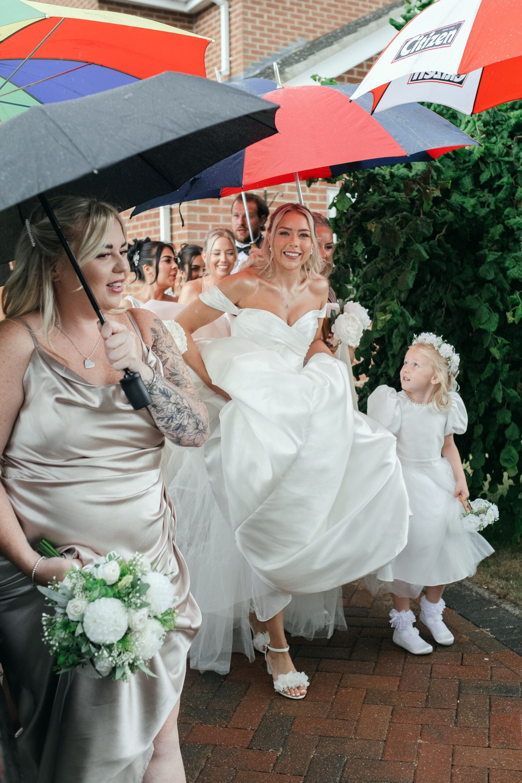 Bride and bridesmaids walking in the rain with umbrellas on their way to St Paul’s Church Gorefield