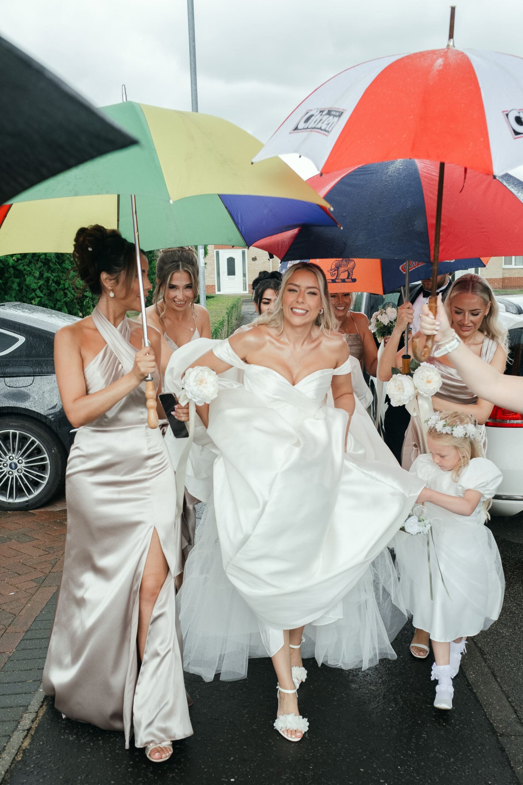 Bride and bridesmaids walking in the rain with umbrellas on their way to St Paul’s Church Gorefield